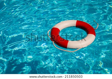 A close up shot of a life guards red and white rescue ring buoy floating in a pool.