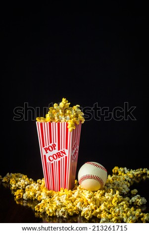 A close up shot of a classic box of red and white striped popcorn box with a baseball isolated against a black background.