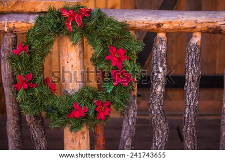 A close up of a Christmas wreath hung on an old west wood hand rail.