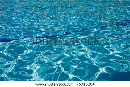 A full frame shot of a cool summer swimming pool with the sun reflecting off the water giving a nice sparkling effect in the cold crisp water. Two blue tiled swim lanes line the bottom of the pool.
