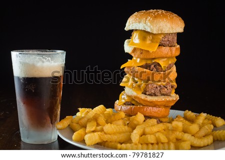 A close up of a five patty cheese burger with fries and a beer.