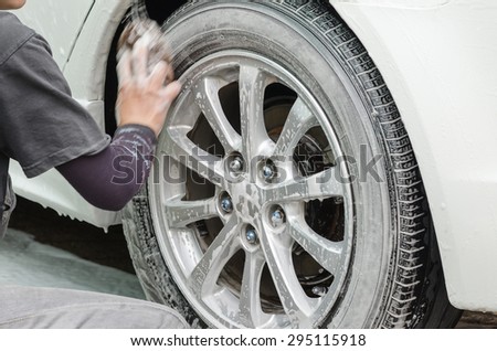 Car washing.A man scrubbing wheels using sponge at car wash station.