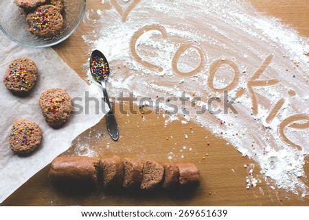 Cookie homemade preparation recipe step ingredients on wooden table flour, cocoa powder, dough pastry, sliced pastry ready to go on baking paper with ready cookies on the side and cookie sign on flour