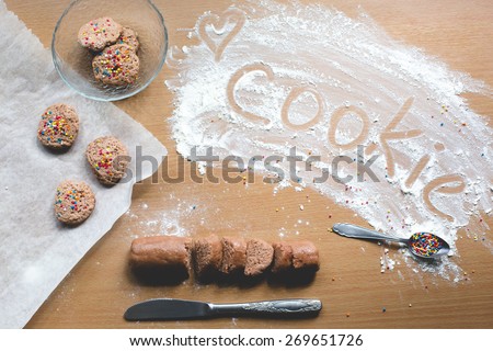 Cookie homemade preparation recipe step ingredients on wooden table flour, cocoa powder, dough pastry, sliced pastry ready to go on baking paper with ready cookies on the side and cookie sign on flour