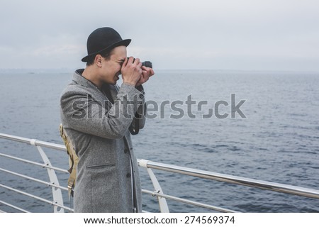 handsome young hipster guy in hat taking picture with film camera of the sea