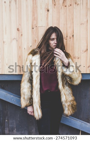 young hipster very beautiful caucasian stylish trendy girl with gorgeous brunette hair is having fun smiling outdoors on a background of the streets and wooden cool backgrounds during windy spring day