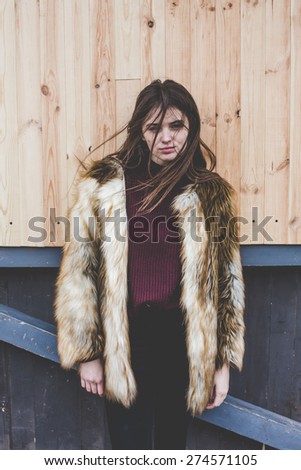 young hipster very beautiful caucasian stylish trendy girl with gorgeous brunette hair is having fun smiling outdoors on a background of the streets and wooden cool backgrounds during windy spring day