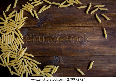 raw pasta texture pattern background frame made of penne pasta on dark rustic wood table with empty space in center for text overhead angle
