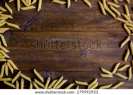 raw pasta texture pattern background frame made of penne pasta on dark rustic wood table with empty space in center for text overhead angle