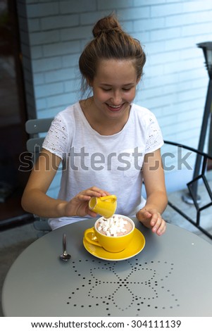 cute beautiful lonely teenager girl drinking hot cocoa with homemade marshmallows in cafe sitting outside