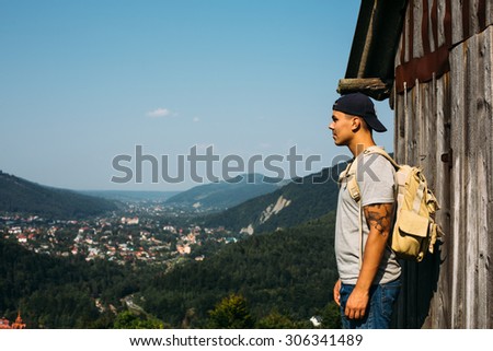 handsome man guy tourist standing alone by the mountain forest landscape during his summer vacation with his backpack