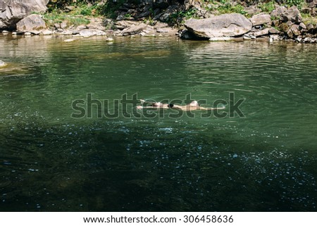 beautiful girl with long curly blonde hair swimming in the river waterfall forest during her summer vacation