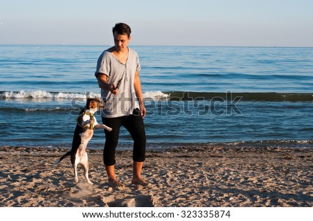 cool trendy stylish sexy handsome happy hipster guy having fun playing with his beagle puppy dog on the beach sea background