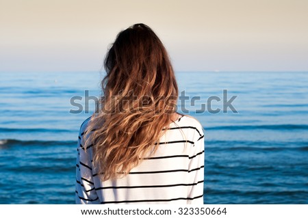 cool trendy stylish sexy blonde lonely girl looking at the calm sea on the sunset with wind in her hair and  seagulls on background