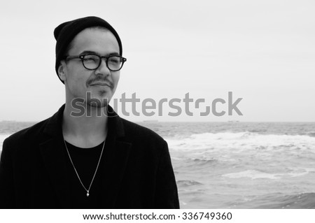 portrait of handsome hipster guy in glasses and hat on hazy cold sea background black and white