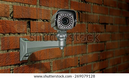 Image of control videocamera the located on a prison wall in beams of yellow lamp illumination.