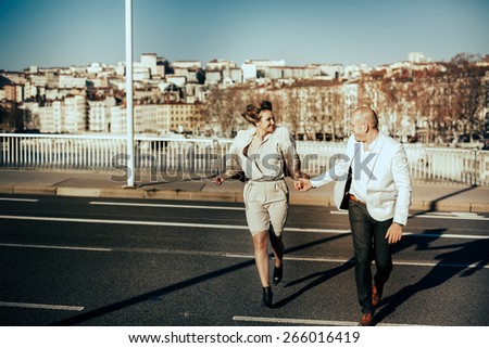 stylish beautiful rich bride and groom walking run on a sunny day on the bridge in the city Lyon on a background of the river and city