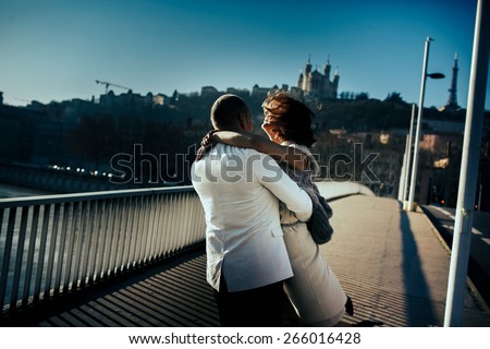 stylish beautiful rich bride and groom walking  and hugging on a sunny day on the bridge in the city of Lyon on a background of the river and city