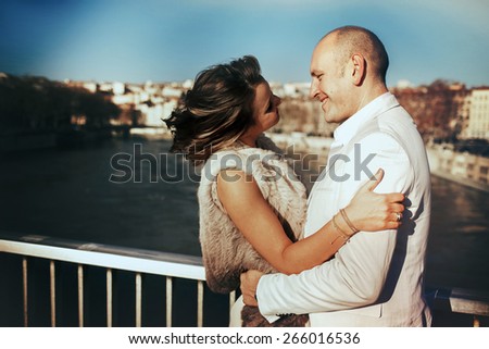 stylish beautiful rich bride and groom walking on a sunny day on the bridge in the city of Lyon on a background of the river and city