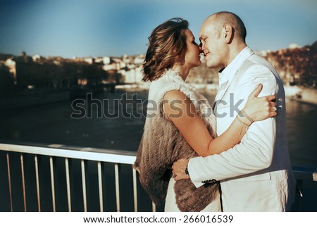 stylish beautiful rich bride and groom kissing on a sunny day on the bridge in the city Lyon on a background of the river and city