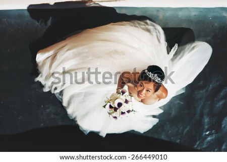 dynamic above  portrait of the asian happy bride in white dress with bouquet of flowers with tiara
