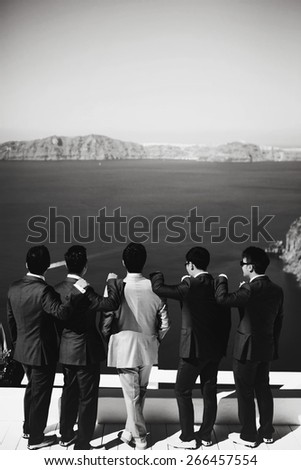stylish rich asian groom with s?hafer and best men watching the  sea on the island of Santorini before wedding ceremony black and white