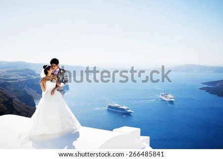 happy stylish asian bride and groom smiling and hugging on background blue sea and sky in island Santorini