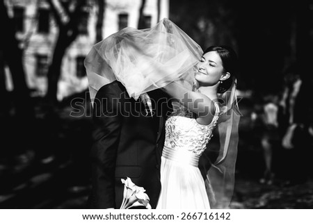 Happy bride is covering her groom with long veil
