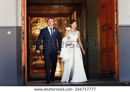 Happily married are walking out of the church with a with a bouquet of calla lilies