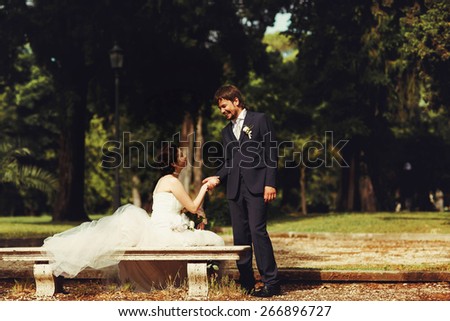 stylish charming rich bride sitting on a bench near stands groom holding hand in the park rome Italy sunny weather