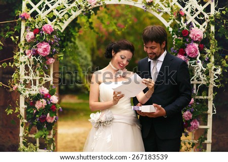 wonderful stylish rich happy bride and groom read marriage certificate at a wedding ceremony in green garden near white arch with flowers Rome Italy