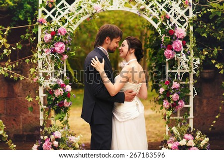 wonderful stylish rich happy bride and groom at a wedding ceremony hugging  look at each other in green garden near white arch with flowers Rome Italy
