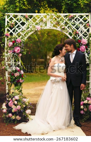wonderful stylish rich happy bride and groom holding hands smiling at a wedding ceremony in green garden near white arch with flowers Rome Italy