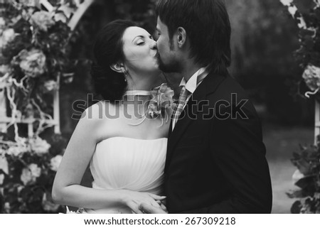 rich stylish happy bride and groom kissing near a white wedding arch decorated with flowers peonies Rome Italy black and white