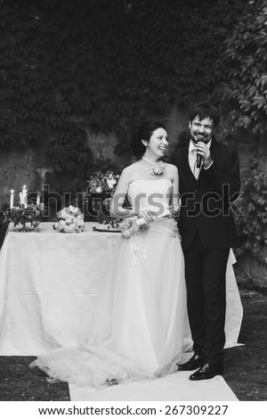 rich stylish happy bride and groom holding hands look at each other near a white wedding table decorated with flowers peonies and candles Rome Italy black and white