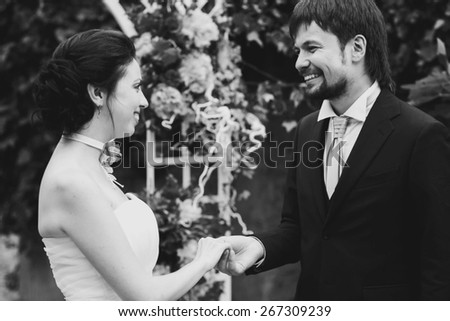 rich stylish happy bride and groom smiling holding hand near a white wedding arch decorated with flowers peonies Rome Italy black and white