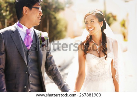 happy stylish asian bride and groom look at each other and holding hands  on street of island Santorini