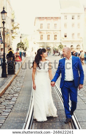 bald groom and bride brunette walking on the streets of the old city by tram tracks Lviv Ukraine