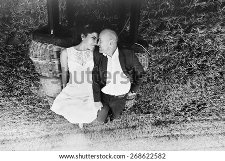 bald groom and brunette bride look at each other lying on basket of balloon  black and white