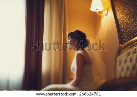 smiling happy bride sitting on a bed in a hotel under the lamp