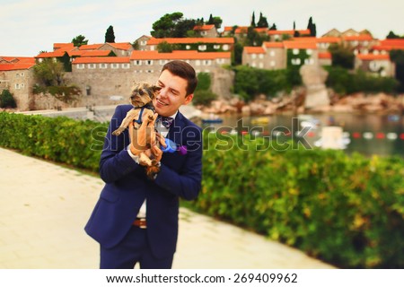happy smiling stylish wealthy groom holding in the hands Yorkshire terrier Montenegro