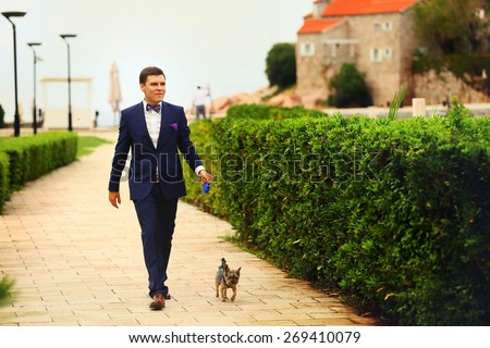 beautiful young rich groom walking on the pavement with Yorkshire Terrier Montenegro