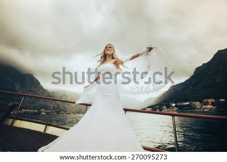 dynamic stylish blonde bride posing on the deck of a yacht on the background of sea and mountains Montenegro