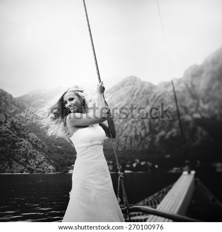 dynamic stylish blonde bride posing on the deck of a yacht on the background of sea and mountains Montenegro