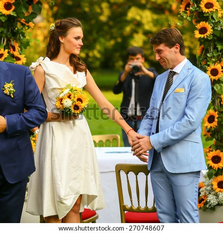 rich stylish groom and bride  holding hand near the arch of sunflowers
