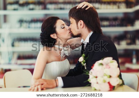 wonderful stylish rich couple bride and groom kissing holding hands on the background  wine shop shelves