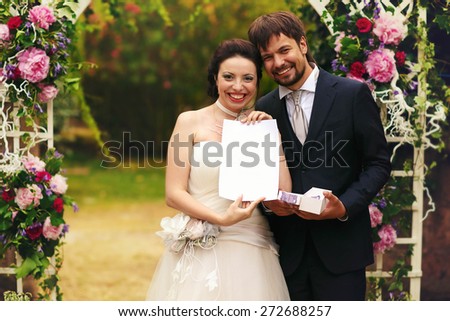 wonderful stylish rich happy bride and groom hold marriage certificate at a wedding ceremony in green garden near white arch with flowers Rome Italy