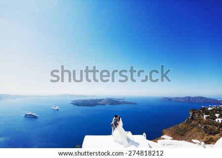 happy stylish asian bride and groom kissing and holding hands on background blue sea and sky in island Santorini