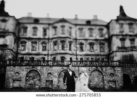 blonde bride and brunette groom walking near  old castle