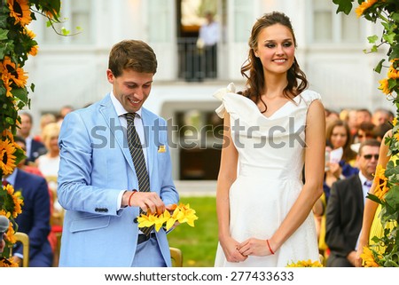rich stylish groom and bride  holding ring near the arch of sunflowers wedding ceremony